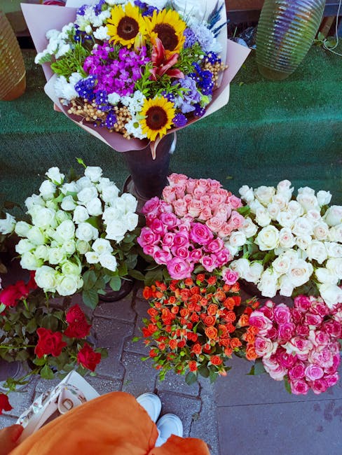 A vibrant display of freshly arranged flower bouquets and a large mixed floral arrangement at a flower stall, featuring a variety of flowers including white and pink roses, red and orange roses, and p