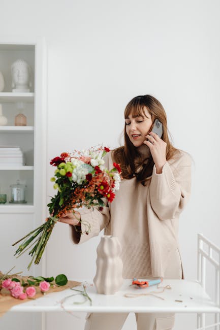 A woman with medium-length brown hair and light skin, dressed in a cream-colored sweater, is holding a large, fresh floral bouquet with a mix of red, pink, white, and green flowers, including roses an